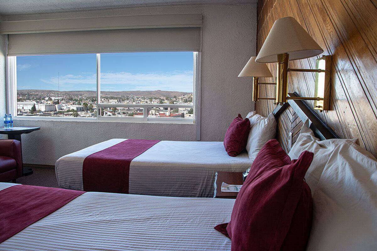 Habitación de hotel con dos camas, vista a un paisaje urbano a través de un ventanal grande y una pared de madera.