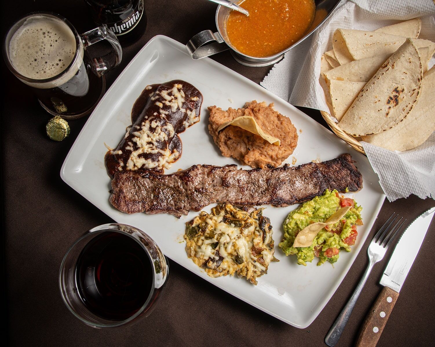Une assiette avec un steak, des haricots, du guacamole et une boisson.