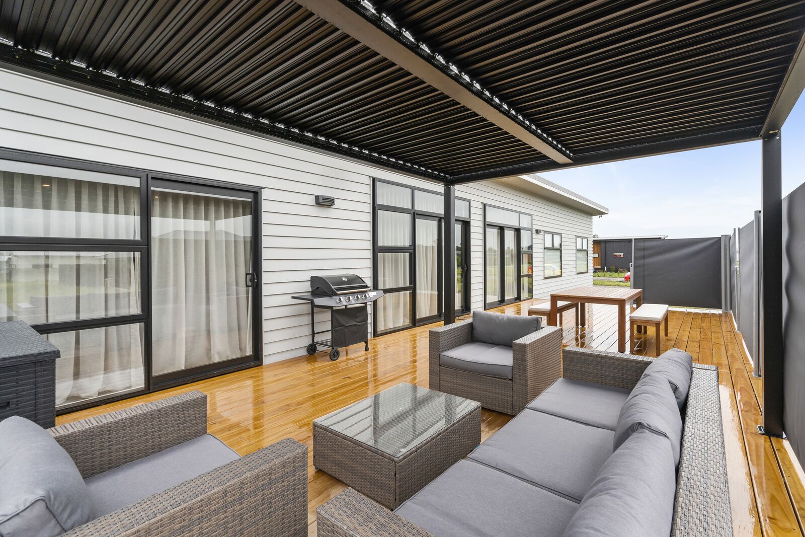 A covered patio with wicker furniture, a grill, and a view of the house.