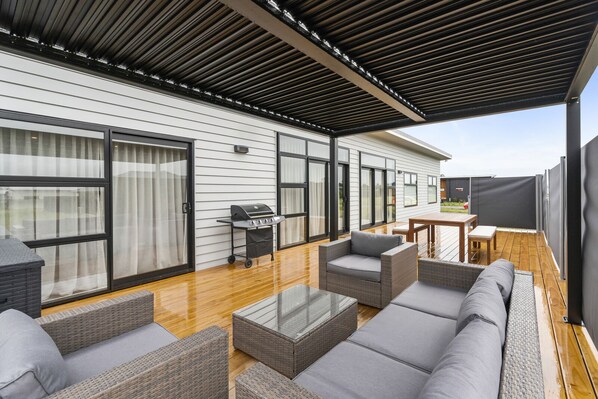 A covered patio with wicker furniture, a grill, and a view of the house.