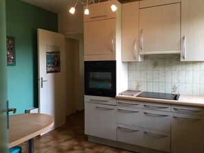 A kitchen with a built-in oven, a microwave, and a sink. There is a door with a poster on it, and a countertop with a drying rack.