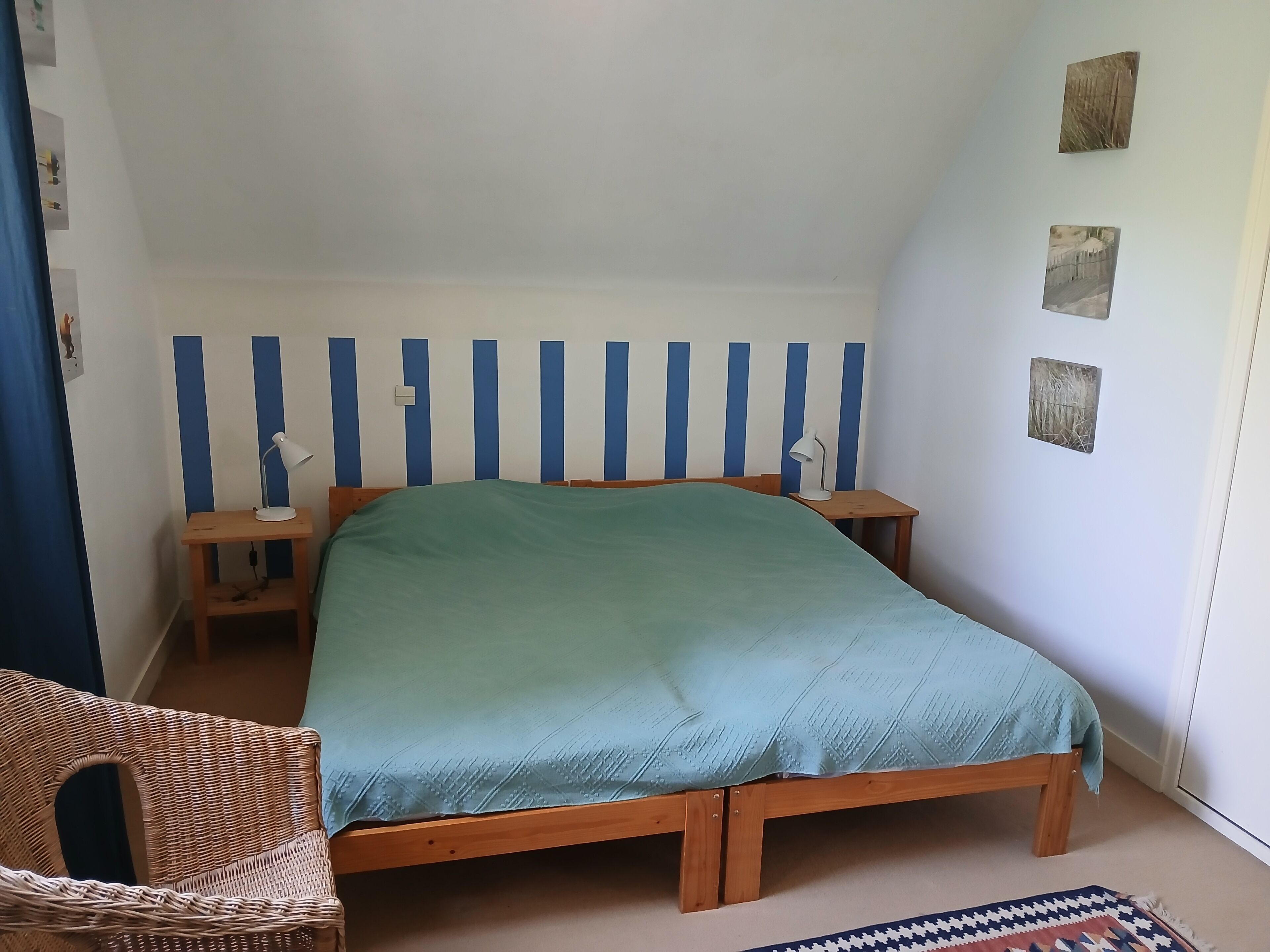 Une chambre à coucher avec un lit simple, deux tables de chevet, une chaise et un mur orné de rayures bleues verticales.