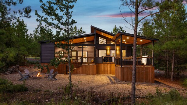 A modern cabin with a deck, outdoor seating, and a fire pit.