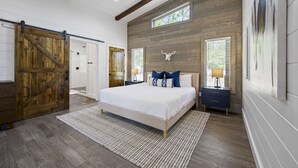A bedroom with a large bed, wooden walls, a ceiling fan, and a sliding barn-style door.