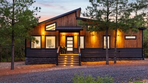 A modern log cabin with a wooden exterior, large windows, and a welcoming entrance with steps.