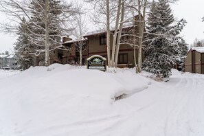 Un camino cubierto de nieve que conduce a un edificio con un cartel que dice "Creekside Condominiums 160 Creekside Dr.".