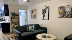 A modern living room with a dark grey sofa, a round coffee table, and a wooden floor. There are two framed artworks on the wall and a kitchen area in the background. - Relax in Ocean Ridge-Near Beach (Boynton Beach)