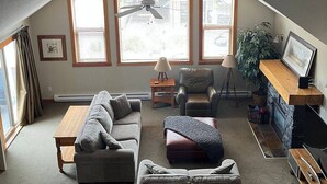 A cozy living room with a sloped ceiling, a fireplace, a sofa, a chair, a small table, and a TV.