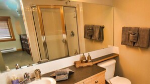 A bathroom with a large mirror, a sink, a toilet, and a shower.