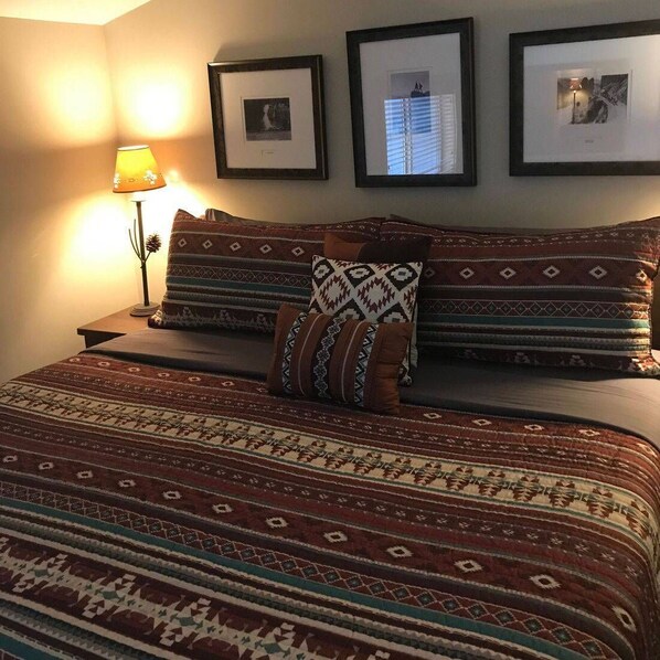 A neatly made bed with patterned bedding and pillows, a bedside lamp, and three framed pictures on the wall.
