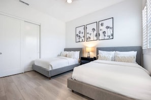 A hotel room with two beds, a white door, and wall-mounted artwork.