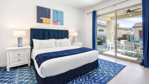A hotel room with a bed, nightstands, a blue patterned rug, and a view of the outdoor patio. - Golfer's Paradise: EV Charger, Private Pool & Putting (La Quinta)