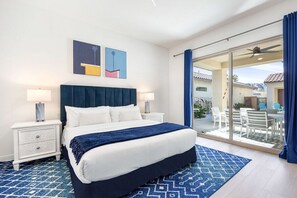 A hotel room with a bed, nightstands, a blue patterned rug, and a view of the outdoor patio. - Golfer's Paradise: EV Charger, Private Pool & Putting (La Quinta)
