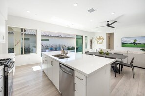 A modern kitchen with a central island, a dining area with a table and chairs, and a large window providing a view of the outdoors.