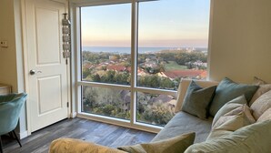 A room with a large window offering a view of a residential area, a sofa with cushions, and a door with a light switch.