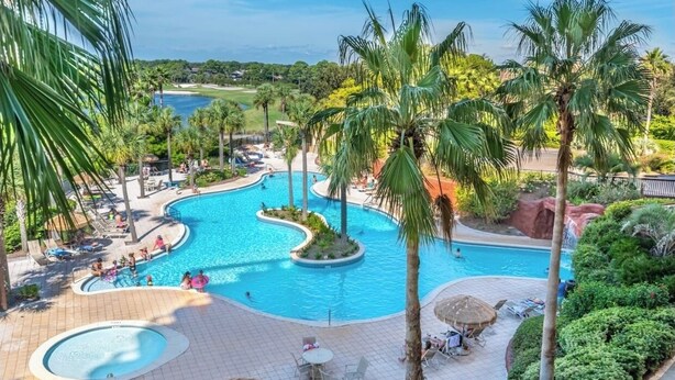 A resort pool area with palm trees, lounge chairs, and a view of the ocean.