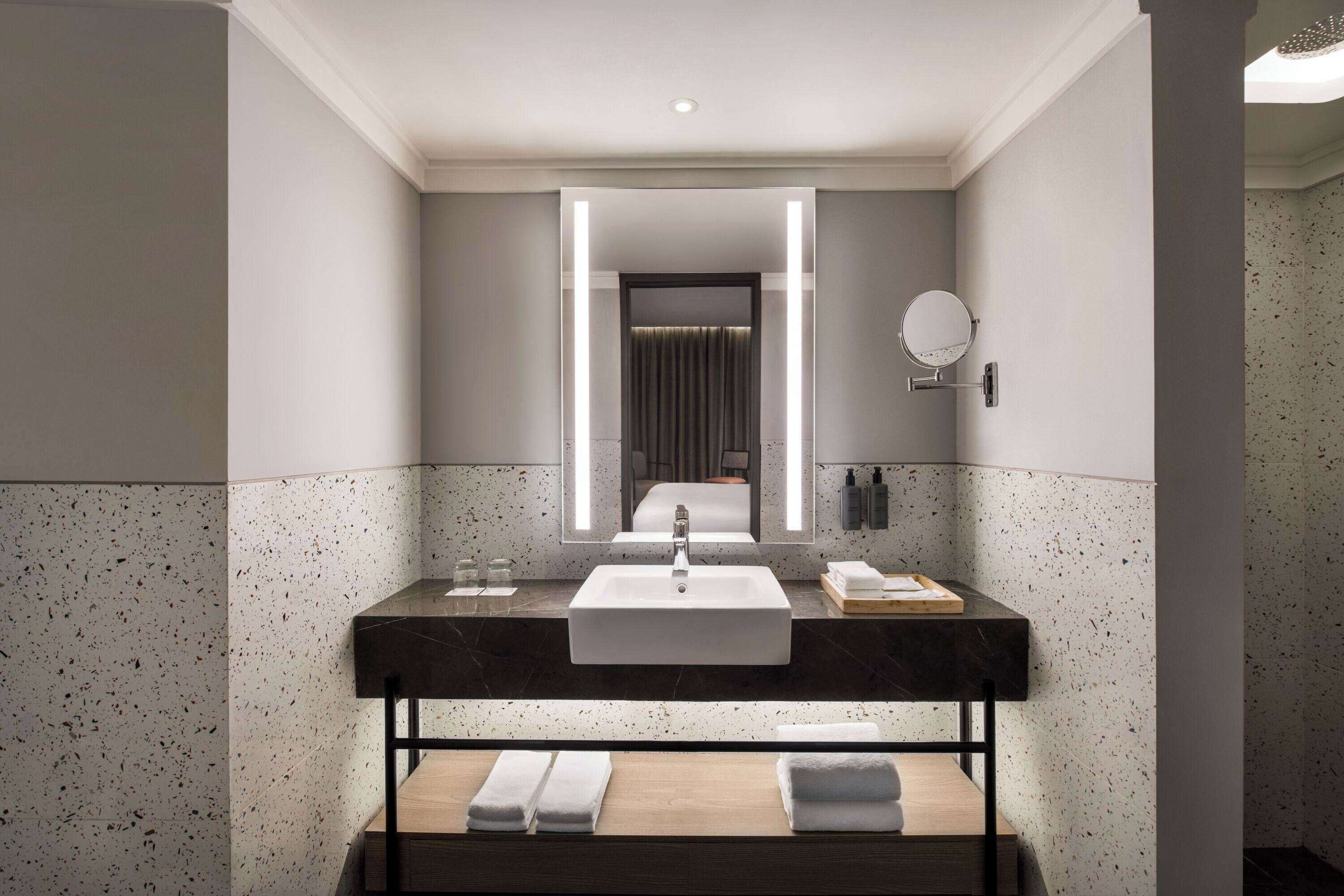 A modern bathroom with a large mirror, a sink, and a towel rack.