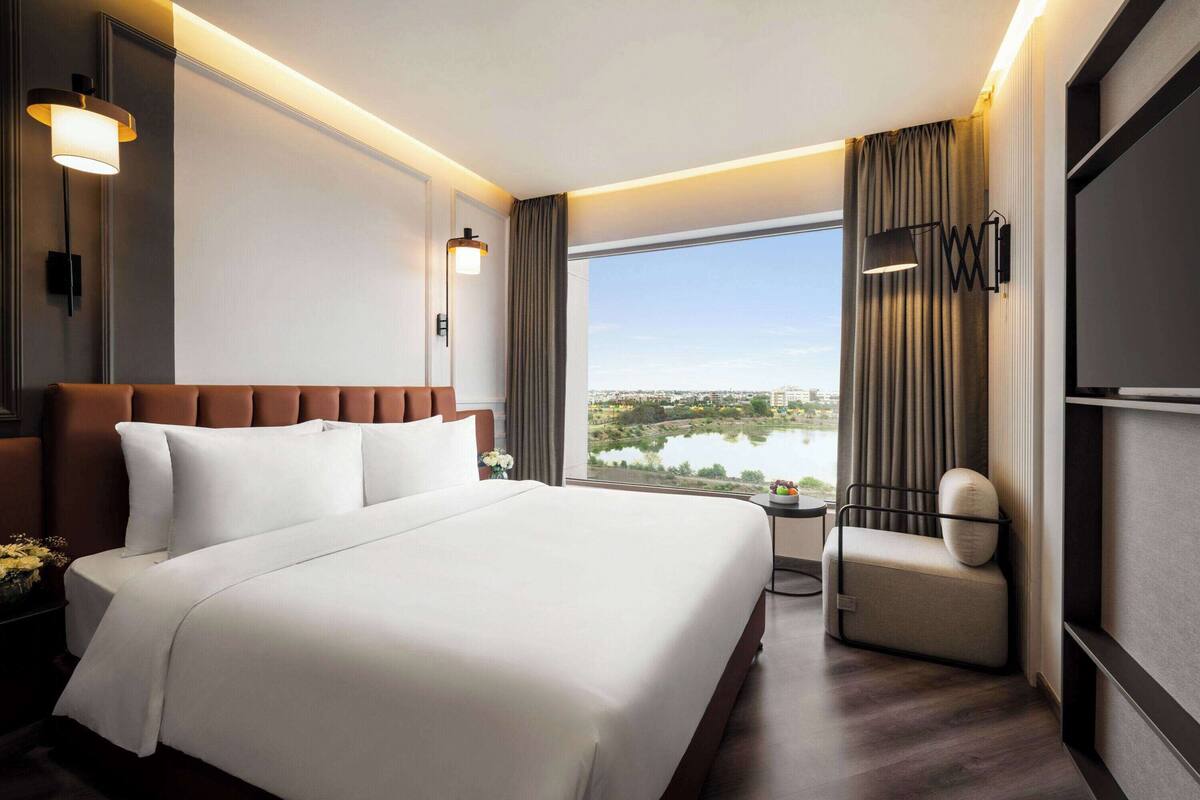 Quarto de hotel com uma cama grande, área de estar e vista para um lago.