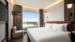 A hotel room with a large bed, a seating area with a chair, a small table, and a view of a lake. - Ramada Encore by Wyndham Indore Nipania (Indore)