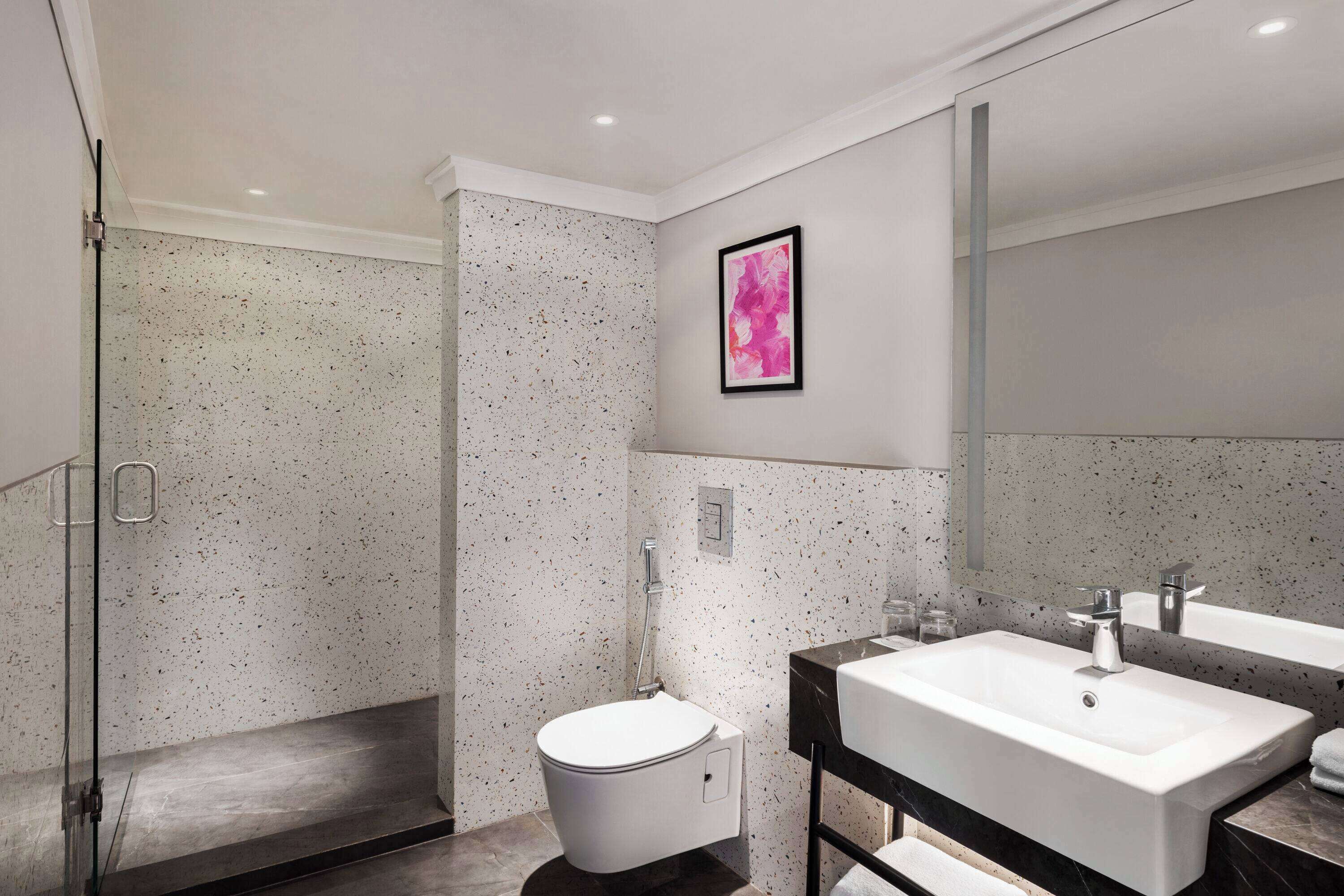 A modern bathroom with a freestanding toilet, a large mirror, and a double sink vanity.