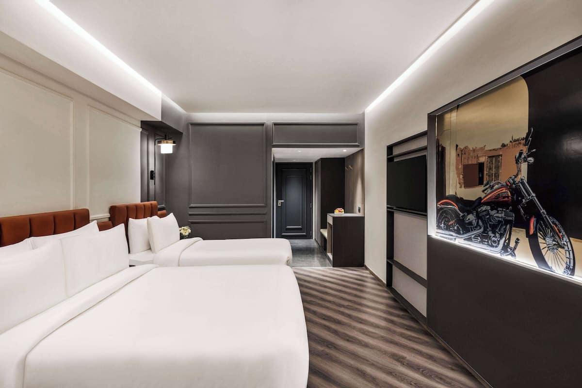 Quarto de hotel com duas camas, um espelho grande e uma televisão na parede.