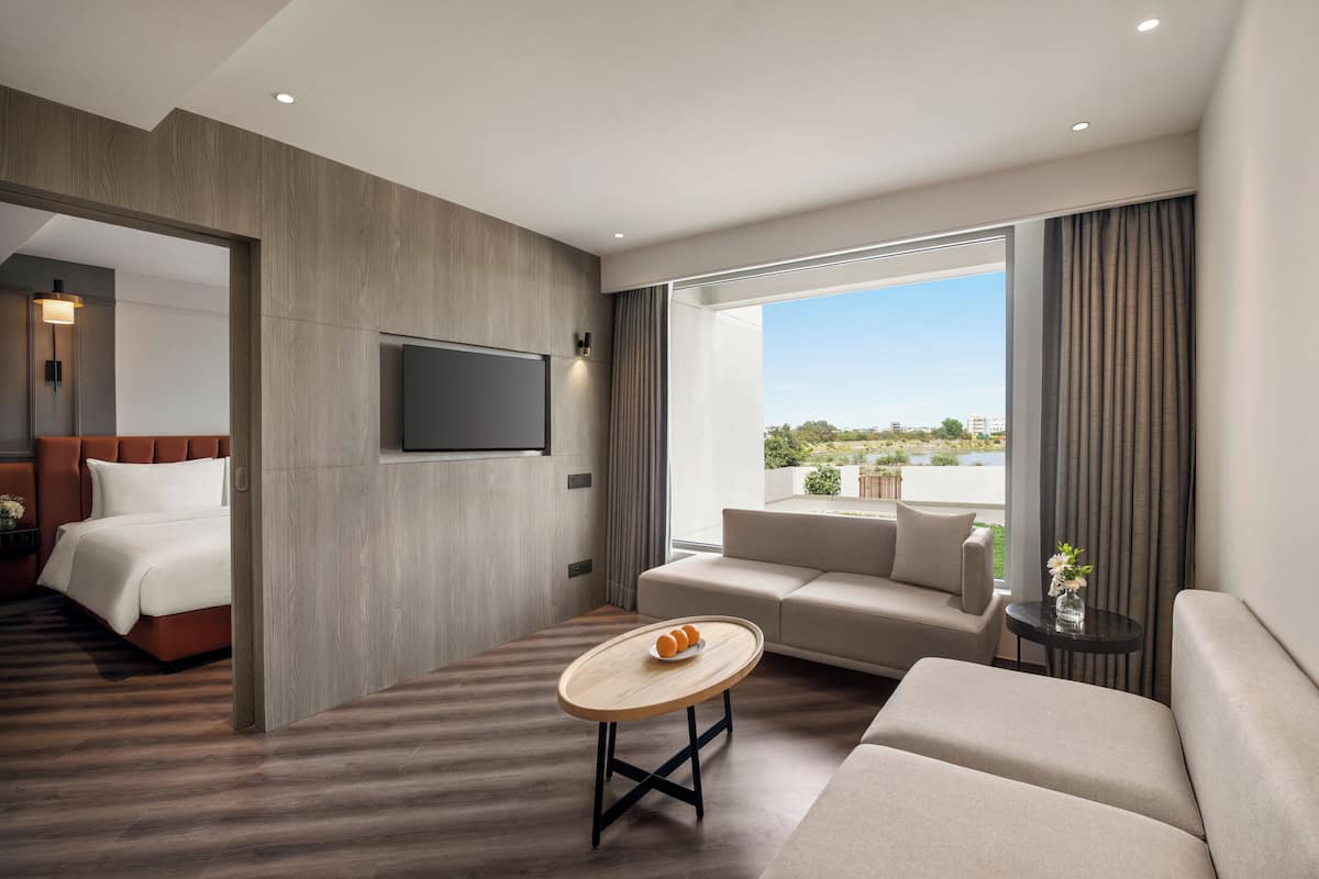 Quarto de hotel moderno com cama, sofá e uma pequena mesa com um vaso.