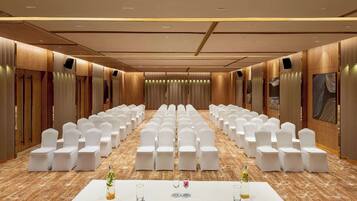 A conference room with rows of white chairs, a long table with nameplates, and a carpeted floor.