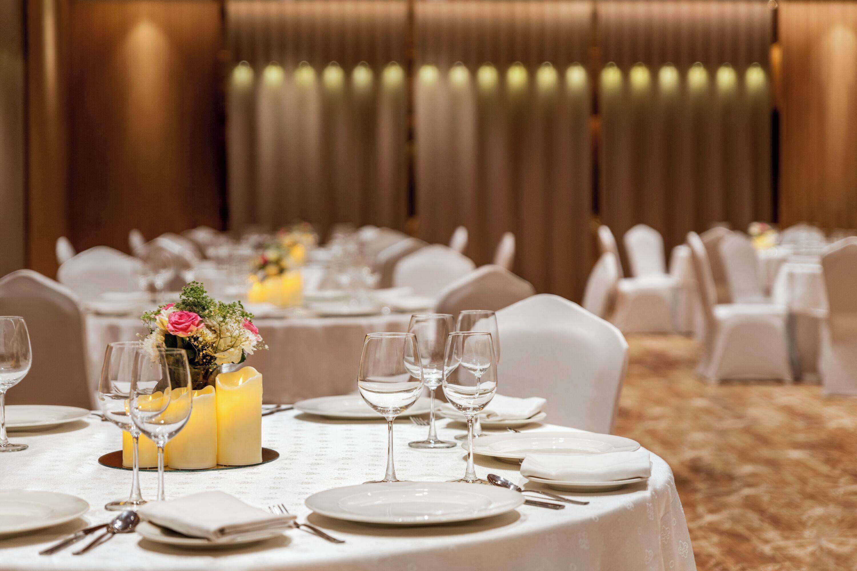 A banquet hall with round tables set for dining, featuring white tablecloths, candles, and floral centerpieces.