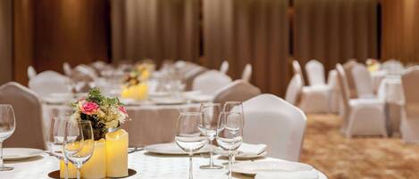 A banquet hall with round tables set for dining, featuring white tablecloths, candles, and floral centerpieces.