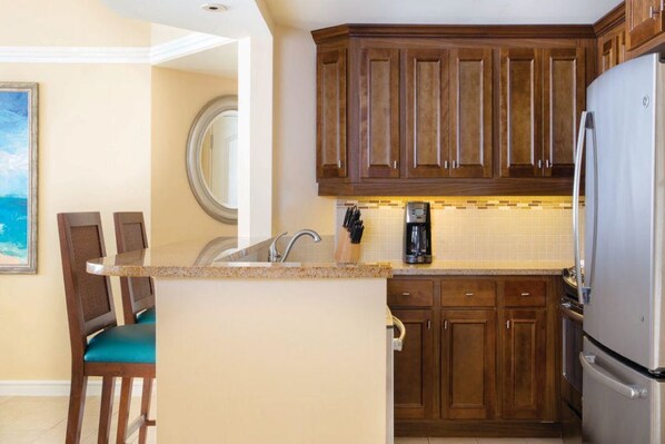 A compact kitchen with wooden cabinets, a stainless steel refrigerator, and a small island with a sink.
