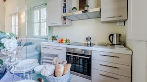 A modern kitchen with white cabinets, a built-in oven, and a coffee maker. There is a dining table with plates and a basket of bread. - Casa Helene in Lucca (Lucca)