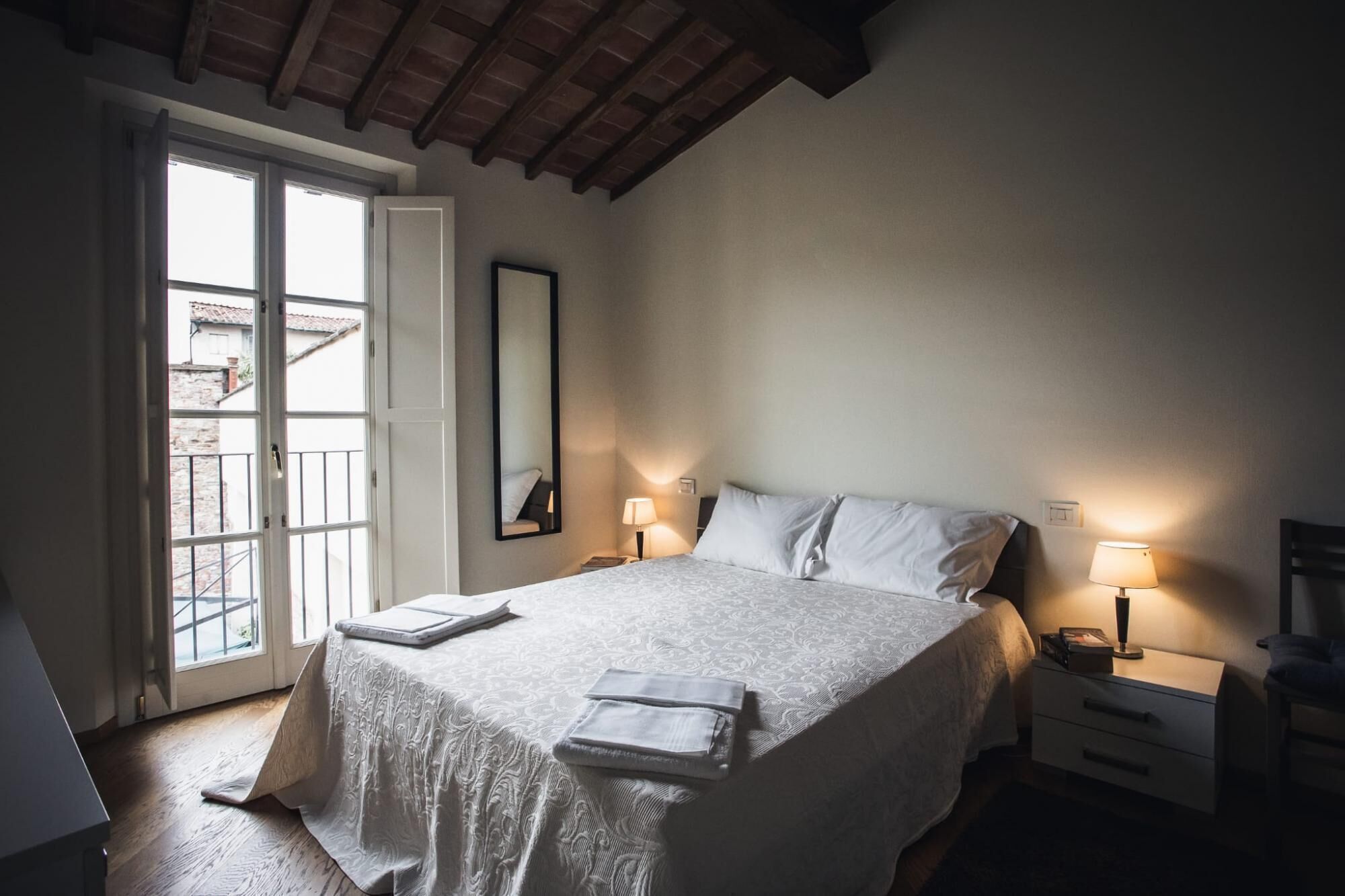 Ein Schlafzimmer mit einem großen Bett, zwei Nachttischen mit Lampen, einem Fenster mit Blick und einer Holzbalkendecke.