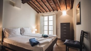 A bedroom with a wooden ceiling, a bed with white linens, a chair, a dresser, and a window with white shutters. - Casa Helene in Lucca (Lucca)