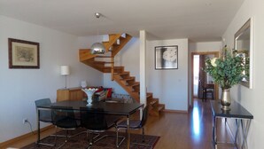 Une cuisine moderne avec un escalier en bois, un coin repas avec une table et des chaises en verre, et un couloir menant à une autre pièce.