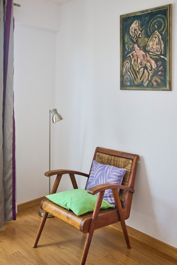 A wooden chair with a cushion and a floor lamp in a room with a painting on the wall.