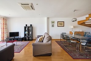 A modern living room with a sofa, TV, bookshelf, dining area, and a staircase. - New apartment in the historic center (Lisboa)