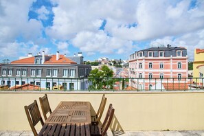 A terrace with a wooden table and chairs, overlooking a cityscape with historic buildings and a clear sky.