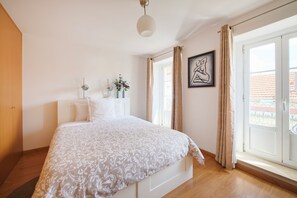 A bedroom with a bed, a bedside table, a lamp, a window with curtains, and a painting on the wall. - New apartment in the historic center (Lisboa)