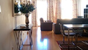 Un vaste espace de vie doté d’un plancher en bois, d’un canapé, d’une table à manger avec des chaises et d’un vase rempli de fleurs.