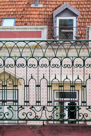 Una cerca metálica con detalles decorativos, un tejado de baldosas y un edificio con ventana y puerta.