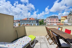 Eine Dachterrasse mit Tisch und Stühlen, einem kleinen Bett und Blick auf die Stadt.