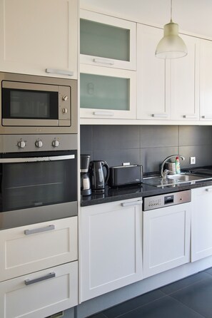 A modern kitchen with white cabinetry, a built-in oven, a microwave, a coffee maker, and a toaster. - New apartment in the historic center (Lisboa)