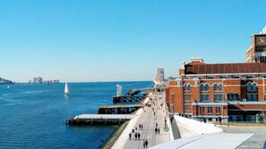 A waterfront promenade with a pedestrian walkway, a bridge, and a sailboat in the distance. - New apartment in the historic center (Lisboa)