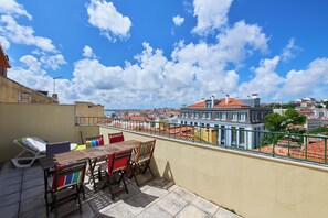 Una terraza en la azotea con una mesa y sillas, con vistas a un paisaje urbano de edificios con tejados rojos.