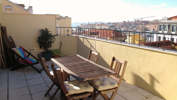 Un balcon avec une table et des chaises en bois, une plante en pot et une vue sur le paysage urbain.