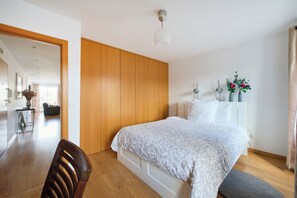 A bedroom with a bed, wooden wardrobe, bedside table, and a view into the living area. - New apartment in the historic center (Lisboa)