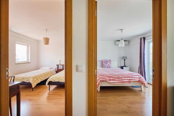 A room with two beds, a window, a bedside table, and a lamp.