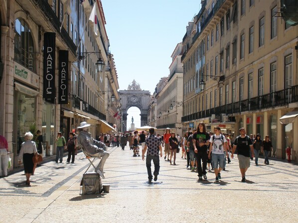 A bustling street with historic architecture, shops, and a prominent archway in the distance. - New apartment in the historic center (Lisboa)