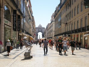 A bustling street with historic architecture, shops, and a prominent archway in the distance. - New apartment in the historic center (Lisboa)