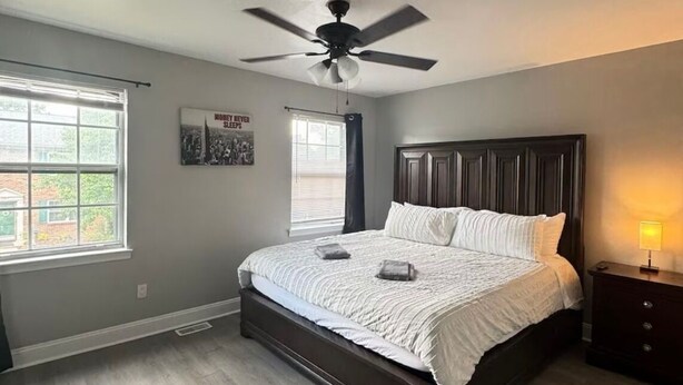 A bedroom with a bed, a ceiling fan, a window, and a nightstand. - 3 Bedrooms Town Home (Charlotte)